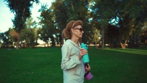 Mature woman going to yoga class outdoors. Active senior enjoying healthy lifestyle. Senior female holding exercise mat while walking at training session. Positive elderly woman with sports equipment — Stock Video