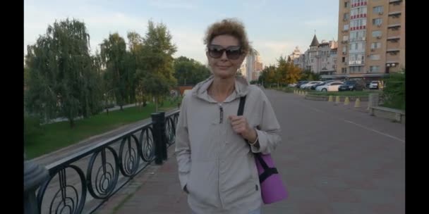 Femme mûre allant à un cours de yoga en plein air. Aîné actif jouissant d'un mode de vie sain. Tapis d'exercice féminin senior en marchant à la séance d'entraînement. Femme âgée positive avec équipement sportif — Video