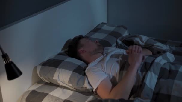 Un uomo preoccupato non può dormire e si gira e si gira a letto, coperto di una coperta di notte con la luce della luna. Il maschio soffre di insonnia. La mattina presto. Disturbo della salute del sonno. — Video Stock