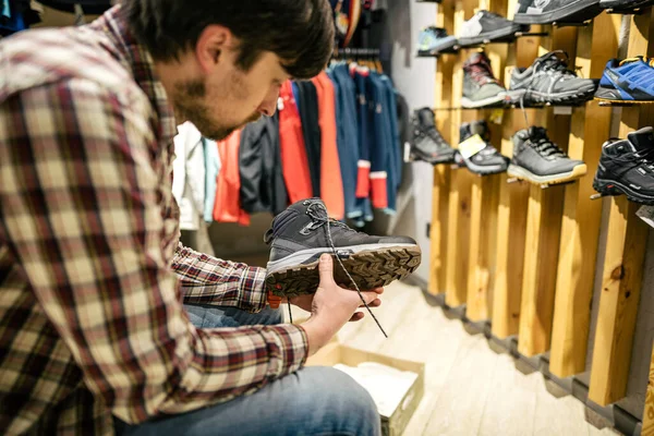 Man shopping in an outdoor store. Male buying mountain boots. Shopper in sports store select hiking shoes. Customer purchase of footwear for adventures. Man trying mountaineering boots at travel shop.