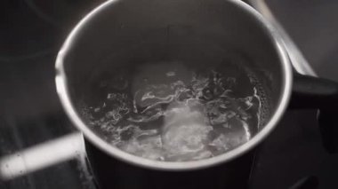 Evde elektrikli ocakta küçük bir tencerede yumurta kaynatmak. Sıcak suda pişen taze beyaz tavuk yumurtaları, yükselen buhar. Beslenme, beslenme, protein kaynağı, sağlıklı yaşam tarzı ve ev yapımı yemek kavramı.