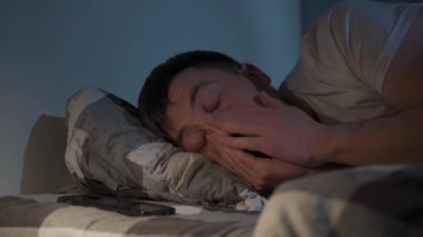 30 yaşındaki bir adam uykusuzluktan muzdarip, geceleri ekose bir battaniyenin altında yatıyor. Yüzüne sürtünüyor ve telefonunu öfkeyle kontrol ediyor, işten önce uyuyamıyor. Ilık sarı lamba parlıyor. 