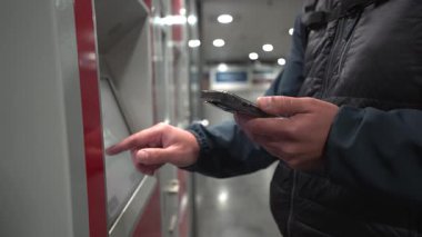 Raveler, Münih 'teki Red DB bilet makinesinden tren bileti alıyor. Adam metro ya da banliyö trenine Deutsche Bahn bileti almak için dokunmatik ekran ve akıllı telefon kullanıyor. Modern seyahat kavramı.