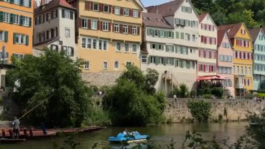 Tuebingen, Almanya. Neckar Nehri kıyısında renkli eski bir kasaba ve kiralık tekneleri var. Universitaetsstadt Tuebingen im Zentrum Baden-Wuerttembergs am Neckar. Teknelerle gezen turistler renkli evlerin yanından geçiyor.