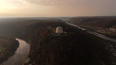 Kelheim, Bavyera, Almanya 'daki Kurtuluş Salonu ile Michelsberg tepesinin panoramik drone görüntüsü. Sahne Tuna Nehri, Ana Tuna Kanalı ve sıcak gün batımı altında dramatik sonbahar yapraklarını gözler önüne seriyor.