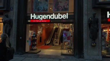 10 Kasım 2025. Münih, Almanya. Odeonsplatz ve Marienplatz yakınlarındaki Hugendubel kitabevi cephesinde aydınlatılmış giriş, kentsel mimari ve yoldan geçen insanlar görülüyor.