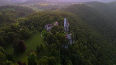Schloss Lichtenstein Wuerttemberg 'in Drone görüntüleri, Reutlingen yakınlarındaki Alman peri masalı kalesi. Manzaralı vadi ve yemyeşil ormanlarla Swabian Jura 'sında çarpıcı bir gün batımı. Maerchenschloss Wuerttembergs