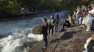 12 Ekim 2025. Münih, Almanya. Beliebte Sehenswuerdigkeit Muenchens die stehende Welle im Eisbach am Englischen Garten. Munchen 'deki Urbanes Surfen die Eisbachwelle ist ein Muss fuer Sportfans.