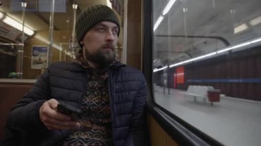 Tarihi bir Muenchen metro vagonunda akşam gezintisi. Kışlık elbiseli bir adam telefonuyla internette geziniyor. Klasik bir Alman U-Bahn treninin içinde tahta paneller ve retro tasarım..