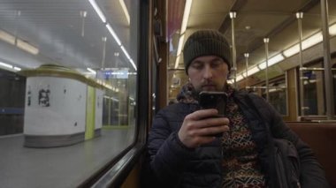 Gece işe gidip gelirken cep telefonu teknolojisini kullanarak banliyö şapkası takan bir adam. Bavyera, Muenchen 'de nostaljik bir Altbau metro vagonunda pencerenin önünde oturuyordum. Otantik şehir hayatı.