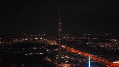 Muenchen 'in yukarıdan panoramik görüntüsü. Olimpiyat Stadyumu ve Fernsehturm 'un karanlık kış gökyüzünün altında insansız hava aracı çekimi. Almanya 'daki Silvester bayramında parlayan şehir ışıkları ve ışık yolları