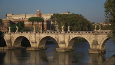 Roma, İtalya 'da Tiber Nehri' ne yayılan Ponte SantAngelo manzarası ve arka planda Castel SantAngelo. Tarihi köprü şehir merkezini Vatikan simgelerine bağlıyor, antik Roma mimarisini sergiliyor