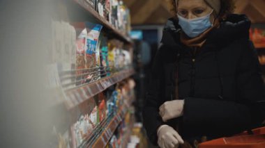 Marketteki yaşlı bir kadın, Coronavirus salgını sırasında tıbbi maske takarak ellerini muayene ederken ürünleri seçiyor ve sosyal mesafeyi koruyor. Konu toplumdaki sağlık güvenliği..
