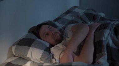 Uykusuzluk, uykusuzluk, uyku bozukluğu. Yatak odasında alacakaranlık, pencereden ay ışığı. Uykusuzluk, sağlık ve dinlenme konsepti. Adam yatakta uyanıkken dönüyor..