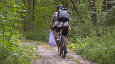 Kirlilik. Ekolojik bir sorun. Erkek bisikletçi kirliliği kaldırdıktan sonra gidon üzerinde çöp torbası taşır. Erkek, ekonomi maratonu sırasında çöp topluyor, plastik şişeleri ve diğer çöpleri temizliyor.