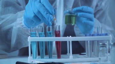 Bir araştırma laboratuarında sıvı örneklerini analiz eden profesyonel bir kimyager. Test tüpü rafında kimyasalları karıştırmak için pipet ve beher kullanmak. İlaç geliştirme ve klinik deney çalışma akışı