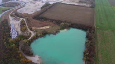Almanya 'da aktif bir kum ocağının yanında açık mavi suyla dolu bir taş ocağının havadan görüntüsü. Sahne, insan sanayisiyle doğal güzelliğin çelişkili olarak yakınlardaki bir otoyol ve sanayi bölgesini içeriyor.