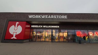 14 Mart 2026. Bergkirchen, Almanya. Engelbert Strauss, profesyonel giyim mağazasının endüstriyel perakende mimarisi. Geniş pencereli koyu tuğla cephe ve parlak kırmızı tabela.