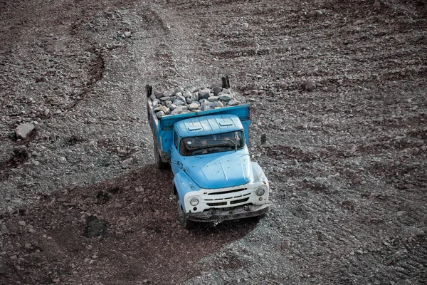 Blue truck transporting granite boulders in the back in an industrial quarry