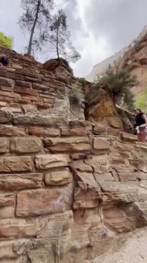 Dikey POV videosu Walters Wiggles 'a tırmanan yürüyüşçüleri takip ediyor. Utah' taki Zion Ulusal Parkı 'nda kaldırımlı bir yol üzerinde bir dizi dik dönüşler. Bulutlu bir gökyüzünün altında kırmızı ve beyaz kumtaşı uçurumlar kulesi.