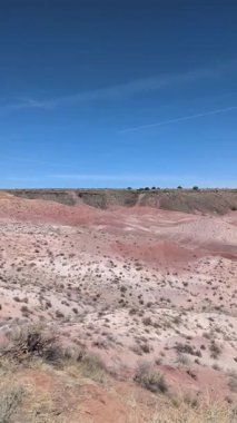 Bu dikey yavaş tava, Arizona 'daki Taşlaşmış Orman Ulusal Parkı' ndaki Boyalı Çöl 'ün geniş renkli manzarasını gözler önüne seriyor. Parlak kırmızı ve pembe tepeler açık mavi bir gökyüzünün altında kurulmuştur..