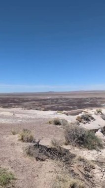 Bu dikey yavaş tava, Arizona 'daki Petrified Forest Ulusal Parkı' ndaki Mavi Orman 'ın eşsiz çorak topraklarını ortaya çıkarıyor. Açık mavi gökyüzünün altındaki manzarada kapalı bir bölgeyi gösteren bir işaret görülebilir..