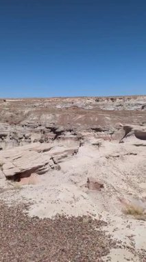Bu dikey yavaş tava, Arizona 'daki Petrified Forest Ulusal Parkı' ndaki Mavi Orman 'ın eşsiz çorak topraklarını ortaya çıkarıyor. Açık mavi gökyüzünün altındaki aşınmış arazide kapalı bir bölgeyi gösteren bir işaret görülebilir..
