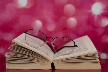 Sayfaların üstünde gözlük olan açık bir kitap. Seçici odak noktaları. Bulanık arkaplan