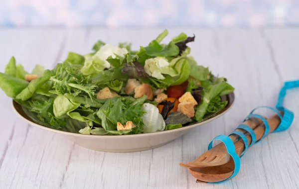 A serving of garden salad, wooden fork and spoon with measuring tape. Selective focus points. Blurred background