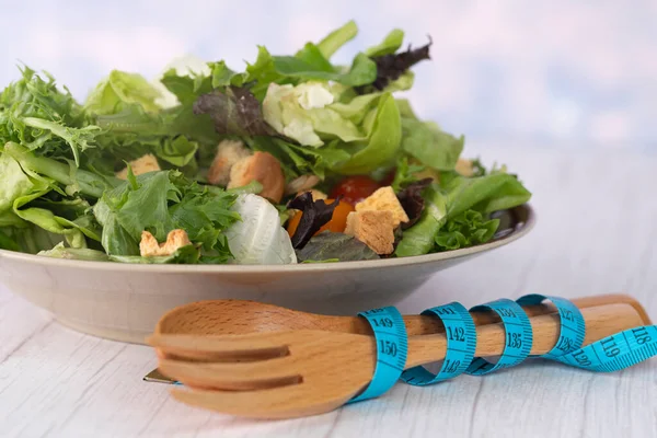A serving of garden salad, wooden fork and spoon with measuring tape. Selective focus points. Blurred background