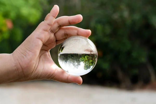Hand holding a clear crystal ball with an upside down view of a landscape. Blurred background
