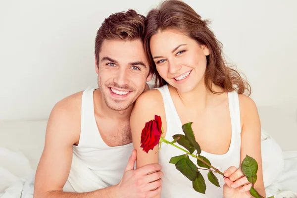 Portrét šťastného páru v lásce sedícího v posteli s červenou růží — Stock fotografie