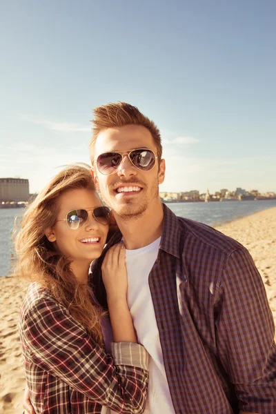 Sonriente pareja enamorada en gafas abrazándose en la orilla del mar — Foto de Stock