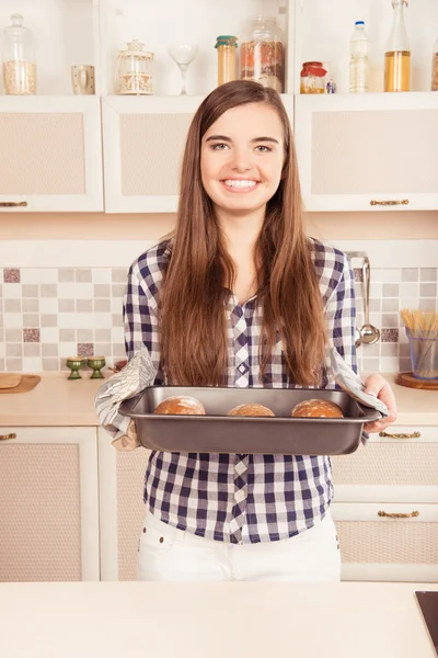 Lachende jonge huisvrouw met een oven-tray met gebakken taarten — Stockfoto