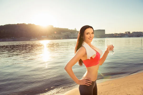 Junge Sportlerin posiert am Strand mit Handtuch und Flasche Wasser — Stockfoto