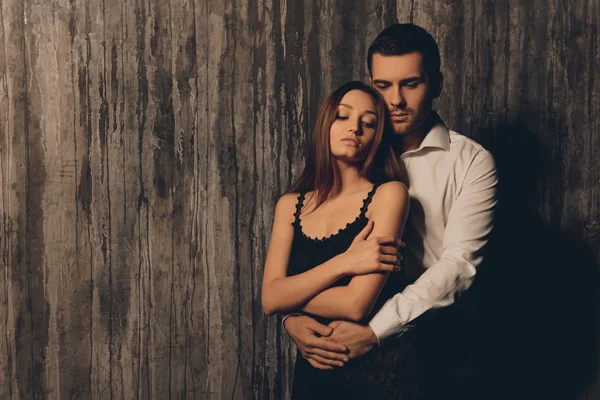 Красивий чоловік обіймає свою сексуальну жінку біля темної стіни — стокове фото