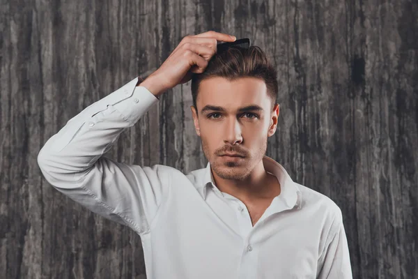 Confident rigid man combing hair on the grey background — Stock Photo, Image