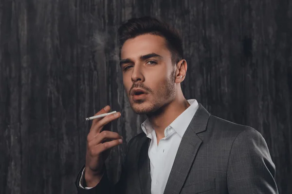 Handome uomo sexy in abito su sfondo grigio fumare una cigare — Foto Stock