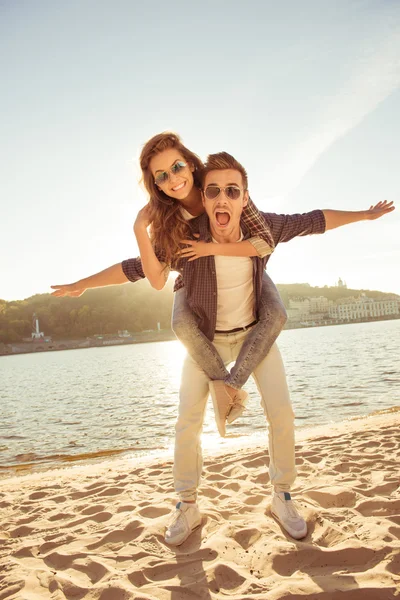 Al atardecer feliz joven a cuestas a su novia en el mar — Foto de Stock