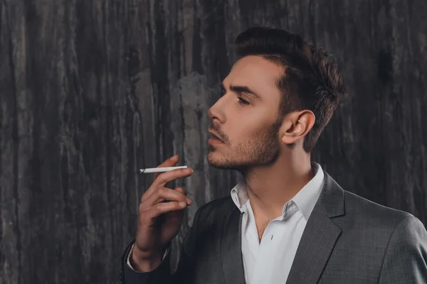Сексуальный жестокий мужчина в сером костюме курит сигарету — стоковое фото