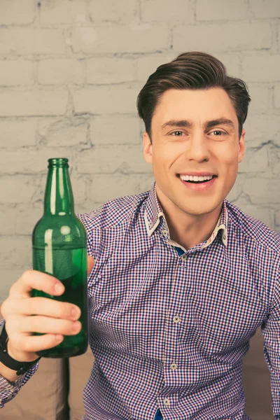 Портрет счастливого человека, сидящего на диване с бутылкой пива — стоковое фото