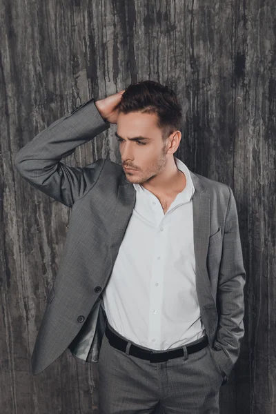 Hombre guapo en traje sobre fondo gris tocándose el pelo —  Fotos de Stock