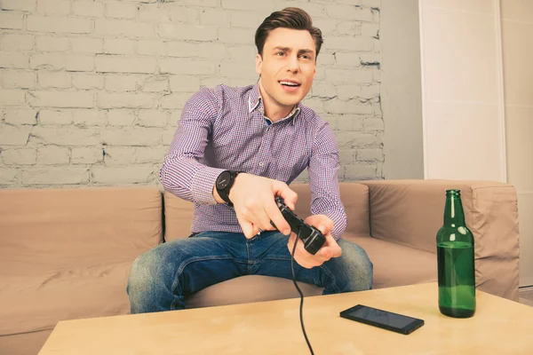 Возбужденный мужчина сидит на диване с бутылкой пива и играет в видео — стоковое фото