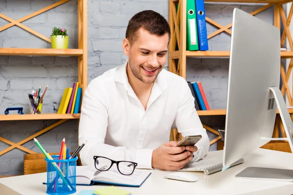 Bonito homem bem sucedido digitando sms em seu local de trabalho — Fotografia de Stock