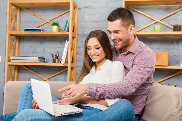 Two happy lovers sitting on couch and working with laptop — Stock Photo, Image