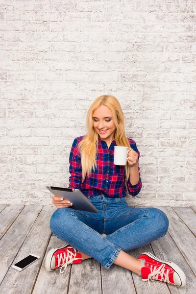 Vonzó lány ül a padló tabletta és csésze kávé — Stock Fotó