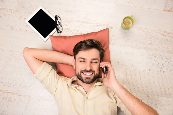 Guapo hombre sonriente tumbado en el suelo y hablando por teléfono — Foto de Stock