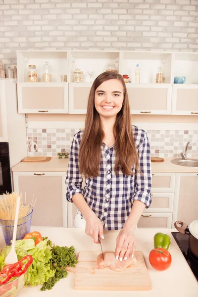 Portret van vrolijke jonge vrouw snijden vlees in de keuken — Stockfoto