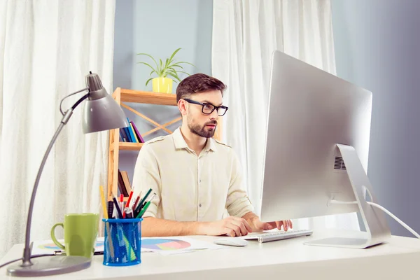 Όμορφος άνδρας στο γυαλιά εργασίας με η/υ και πληκτρολογώντας στο γραφείο — Φωτογραφία Αρχείου