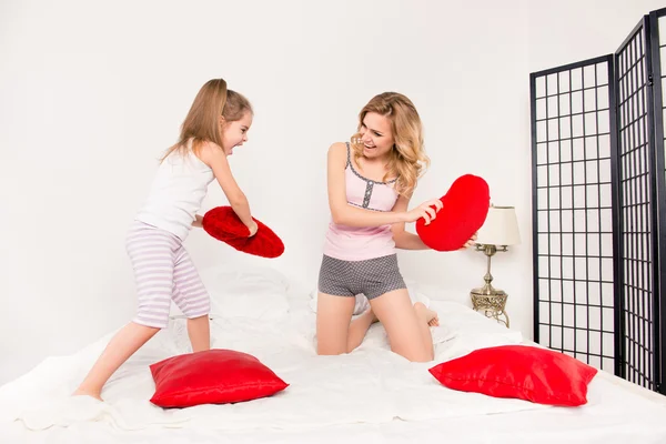 Мама и ее дочь играют на кровати и дерутся с подушками — стоковое фото